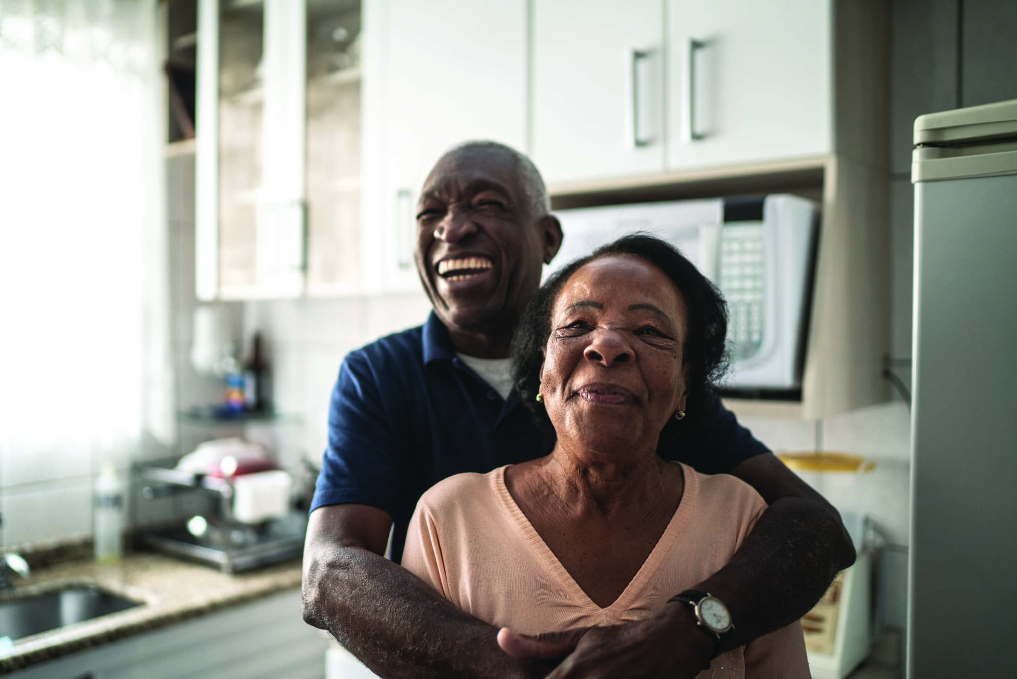 African American older couple hugging and smiling in kitchen
